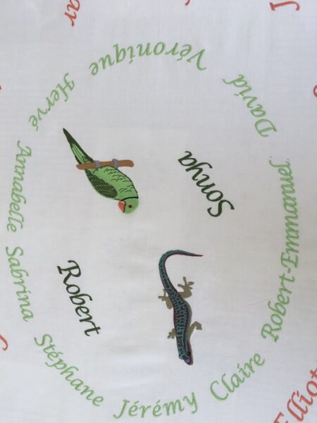 Nappe brodée de prénoms et d’un lézard et d’un perroquet au centre