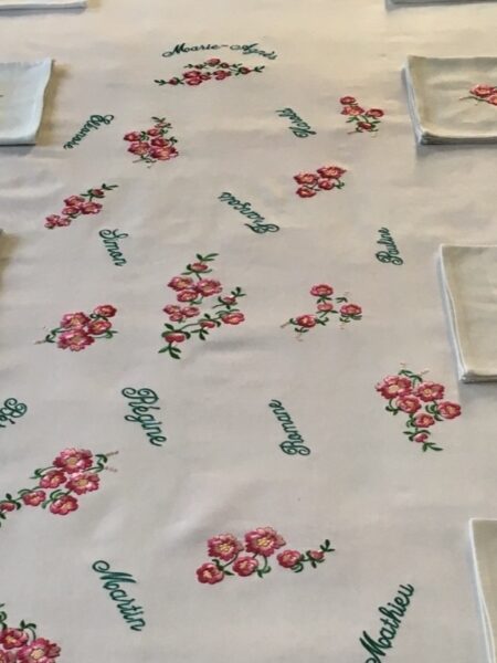 Nappe blanche brodée de fleurettes roses entourées de prénoms