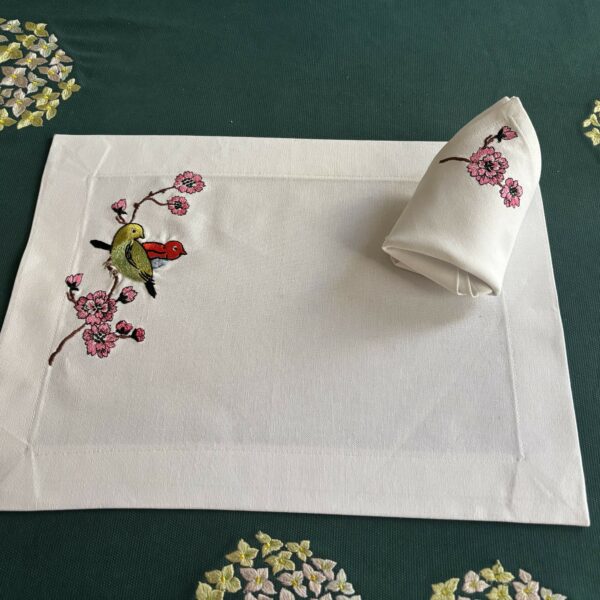 L'art de recevoir : un set de table en lin blanc brodé d'une branche de cerisier où repose un couple d'oiseaux aux finitions délicates pour sublimer vos dîners.