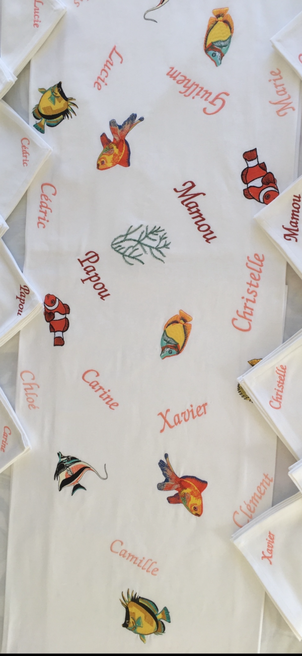 Zoom sur les détails des broderies : poissons tropicaux et prénoms s'entremêlent avec finesse.