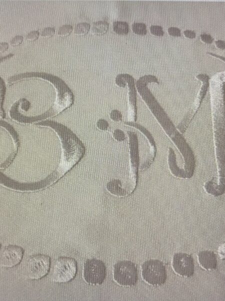 Un grand monogramme brodé au centre d&rsquo;une nappe blanche.